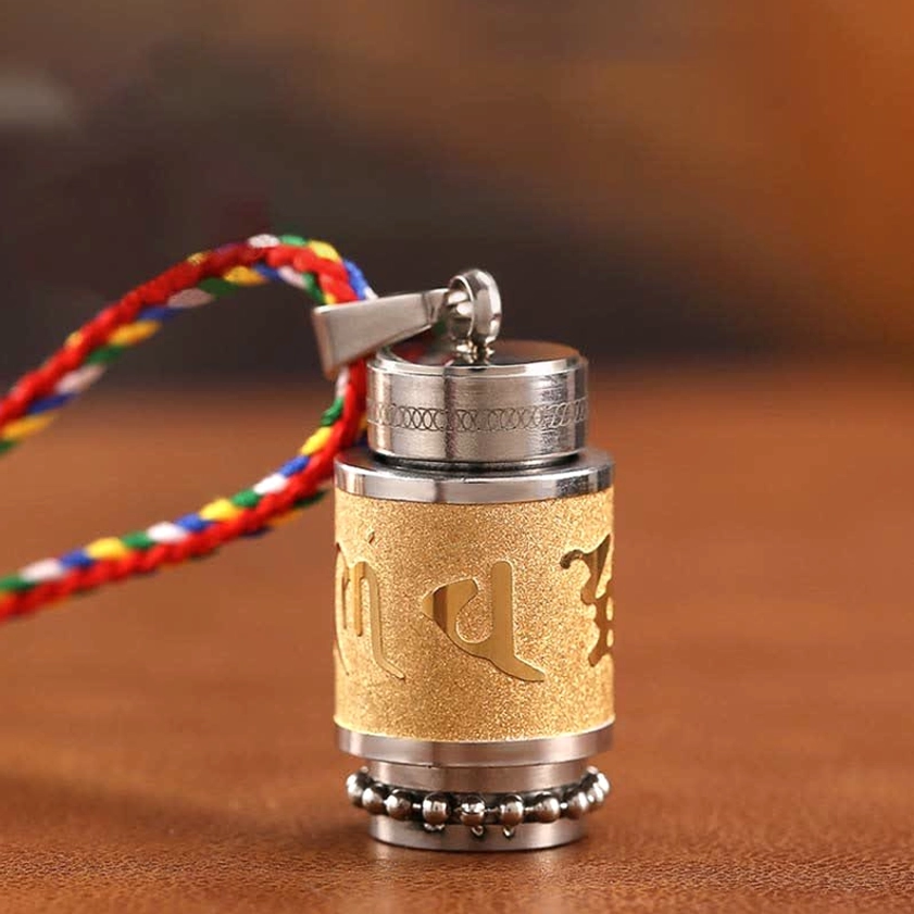 Om Mani Padme Hum titanium steel buddhist amulet pendant close-up front view with frosted gold mantra band and colorful woven lanyard