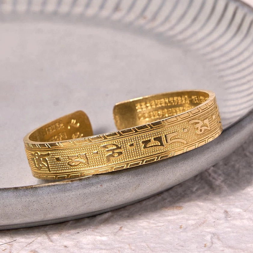 Om Mani Padme Hum brass bracelet showing inner surface engraving with full mantra text visible on ceramic plate background, oblique angle view