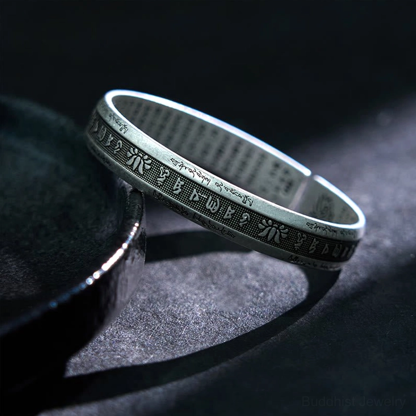 Vintage silver open-ended cuff bracelet with sacred text and floral patterns, side view on black ceramic plate