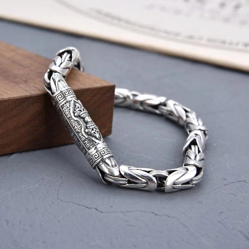 Vintage-style silver Buddhist bracelet featuring carved barrel charm and twisted wheat chain design, three-quarter view