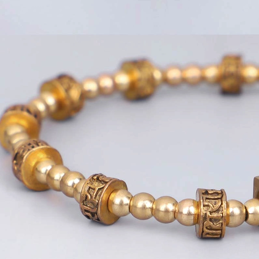 Close-up macro view of carved cylindrical bronze mantra beads and smooth round stone beads on Buddhist bracelet