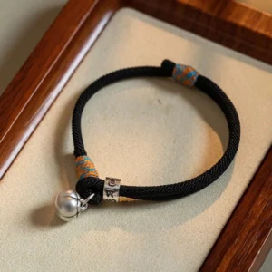 Black handmade Om Mani Padme Hum braided Buddhist bracelet with sterling silver mantra bead and persimmon charm on wooden tray