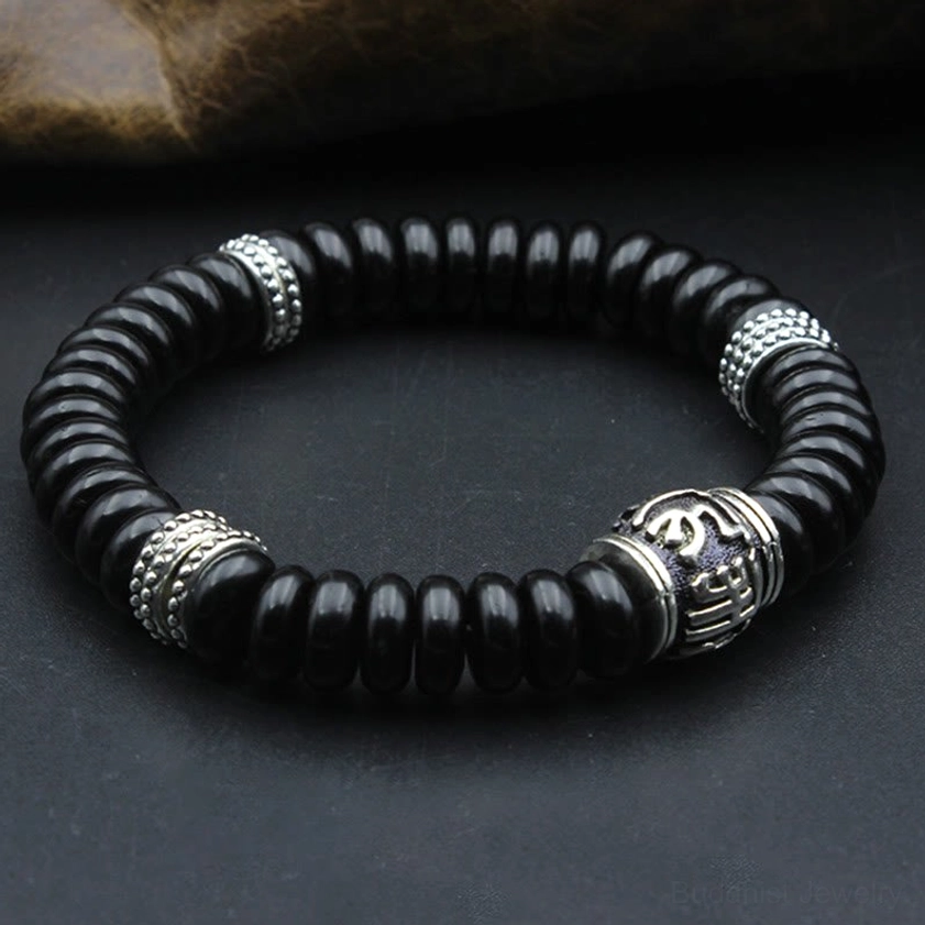 Matte black coconut shell mantra bracelet with silver metal accents, overhead flat lay on dark fabric