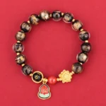 Black Liuli glass Buddhist bracelet with Om Mani Padme Hum charm, lotus pendant, and Fu character gourd on red background