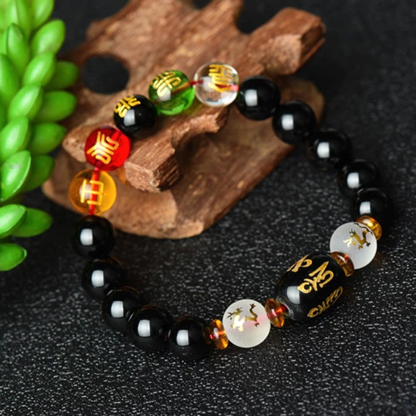 Sacred Buddhist prayer bracelet featuring black onyx beads, gold spacers, and engraved mantra focal bead on wooden craft background