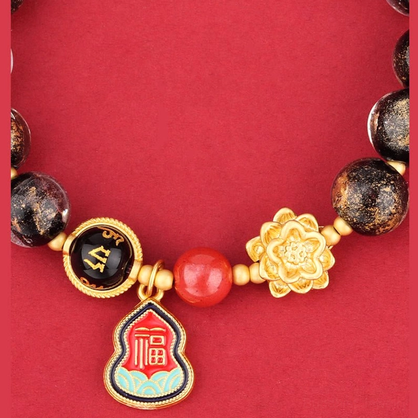 Close-up detail of Buddhist bracelet showing speckled glass beads, gold lotus flower charm, and sacred symbols