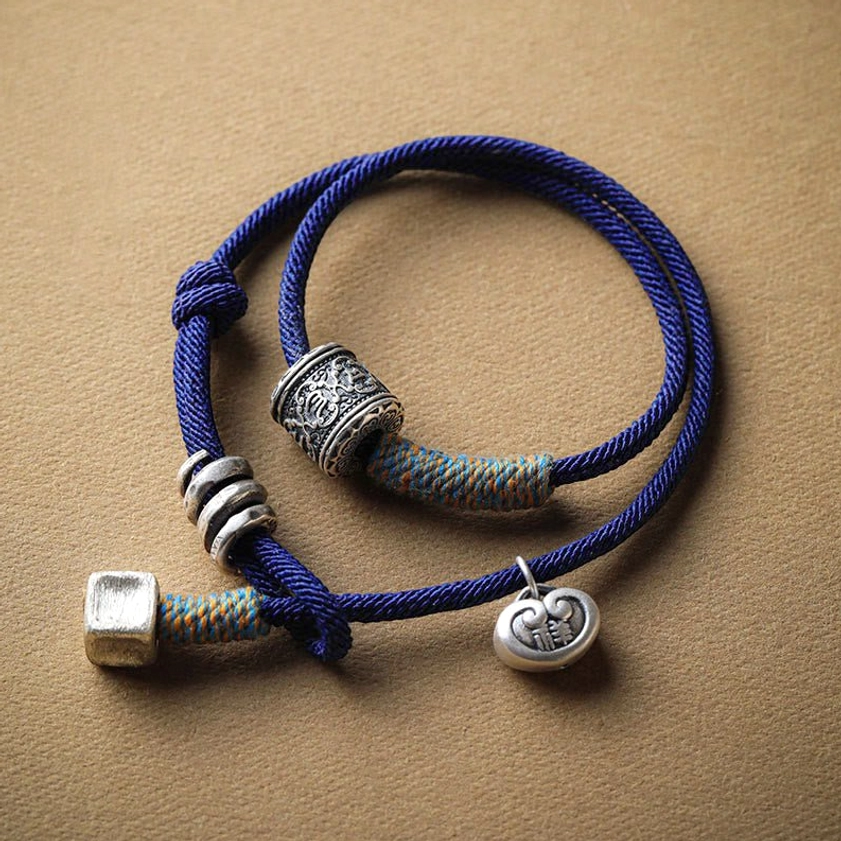 Om Mani Padme Hum carved bracelet with dark blue braided rope and silver beads, flat lay top view