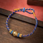Blue and gold Om Mani Padme Hum woven Buddhist bracelet with engraved mantra bead on wooden surface