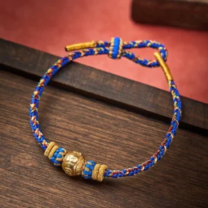 Blue and gold Om Mani Padme Hum woven Buddhist bracelet with engraved mantra bead on wooden surface