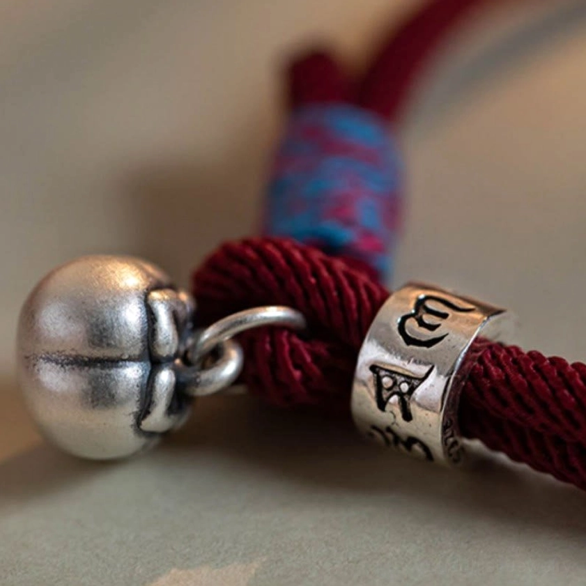 Macro close-up of sterling silver persimmon bell charm and engraved Om Mani Padme Hum bead with red rope