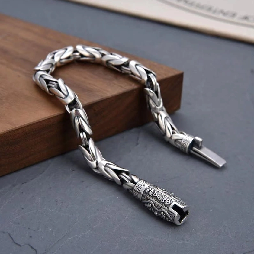 Buddhist mantra chain bracelet showing carved Om Mani Padme Hum clasp with push-tab fastener on wooden surface