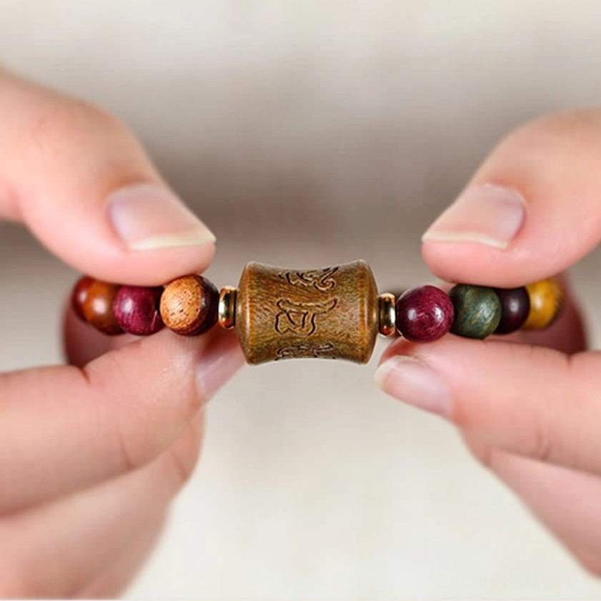 Close-up detail of multicolor sandalwood bracelet held in hand, showing carved mantra bead and mixed wood tones