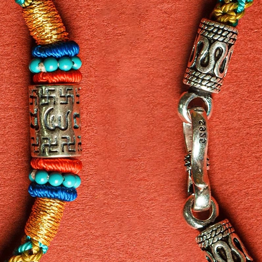 Close-up detail of Buddhist bracelet showing turquoise beads, red woven wraps, and silver engraved tube with mantra