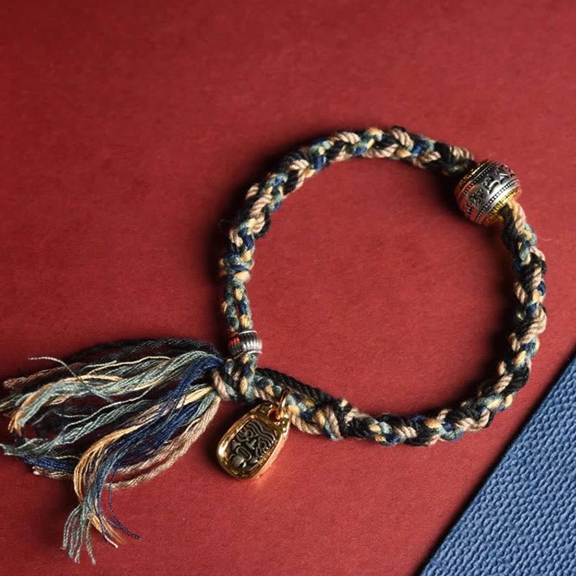 Buddhist prayer bracelet with multicolor woven rope, engraved metal charm and tassel pendant, side flat lay view