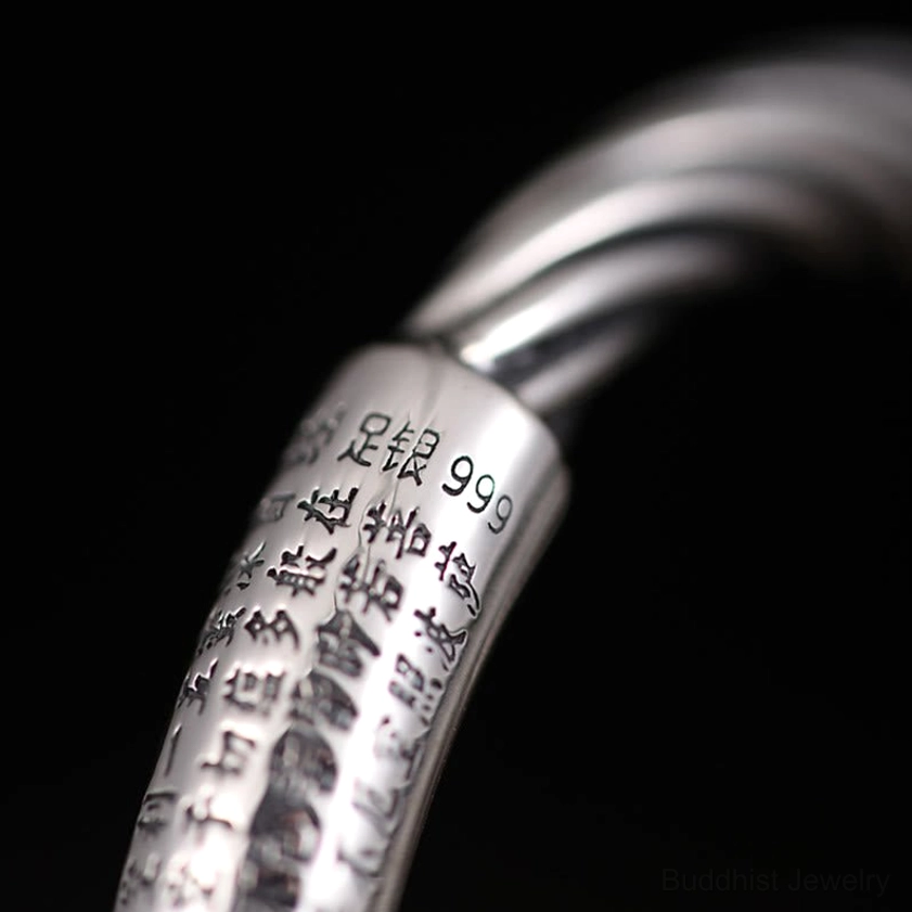Close-up macro photography of hand-engraved Buddhist mantra characters on copper cuff bracelet showing intricate text detail and twisted rope pattern
