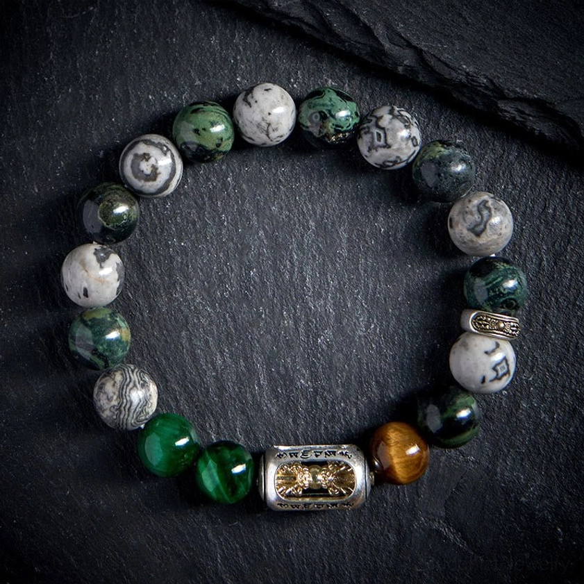 Multi-stone Buddhist protection bracelet with natural healing gemstones flat lay on black fabric background showing metal spacer bead and engraved sacred text