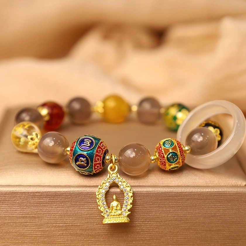 Handmade Buddhist prayer bracelet with gray agate beads, enamel mantra beads, and golden Buddha charm on soft fabric background, top-down view
