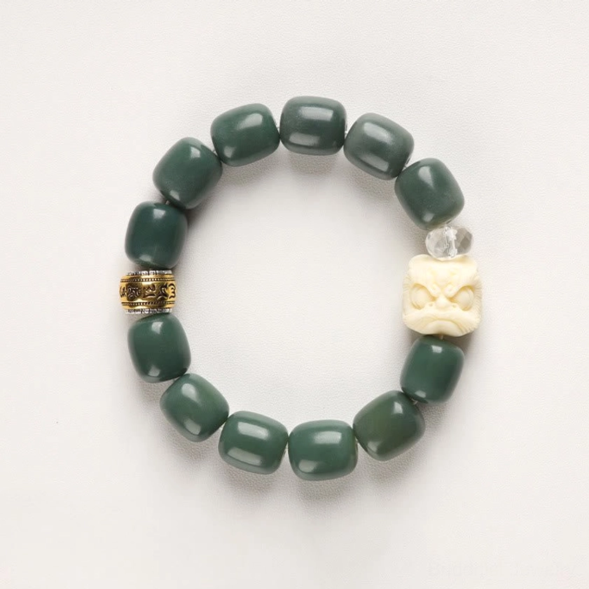 Buddhist bracelet flat lay top view showing dark green bodhi seed beads, ivory lion head, crystal accent, and engraved metal spacers