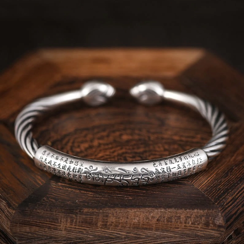 Flat lay top-down view of Buddhist mantra cuff bracelet showing detailed engraved Om Mani Padme Hum characters on copper band with rounded end caps