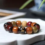 Multi-wood Om Mani Padme Hum Buddhist bracelet displayed on white decorative tray, featuring mixed natural wood tones with golden engraved mantra bead
