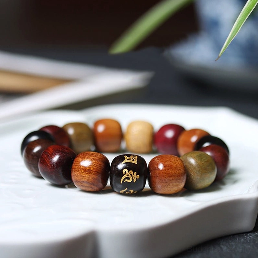 Multi-wood Om Mani Padme Hum Buddhist bracelet displayed on white decorative tray, featuring mixed natural wood tones with golden engraved mantra bead