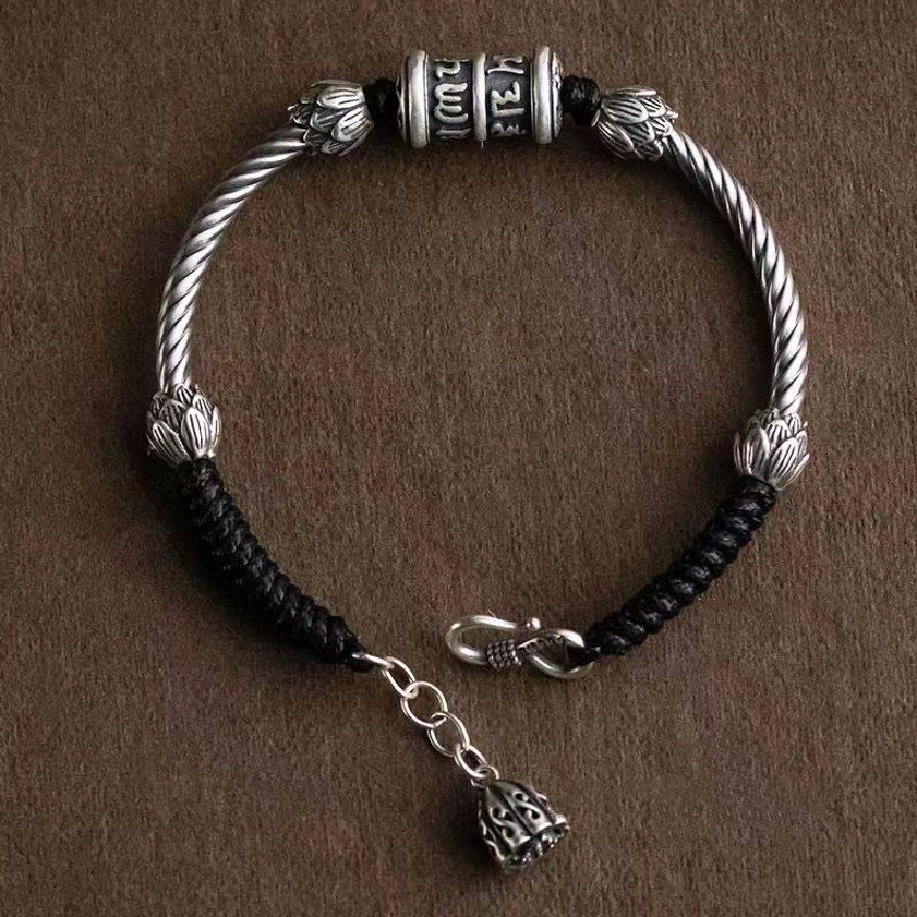 Buddhist mantra bracelet flat lay with extender chain and lotus pendant charm, showing braided cord and silver-tone mantra cylinder