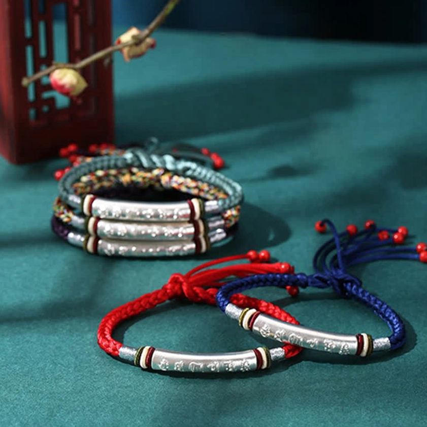 Stacked collection of sterling silver bangles and red blue Buddhist string bracelets with engraved sacred text silver tubes