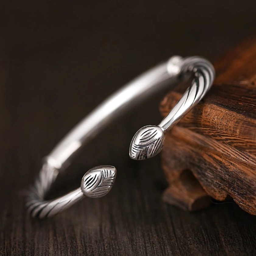Low angle side view of Om Mani Padme Hum copper bracelet featuring decorative leaf-shaped end caps and twisted band texture on wooden surface