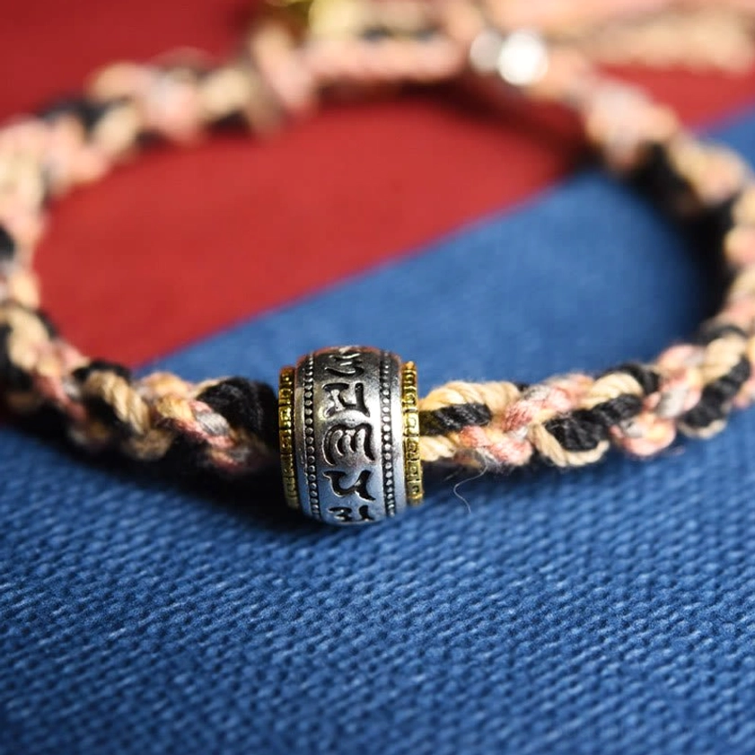 Handmade Buddhist mantra bracelet macro close-up showing dual-tone woven rope and silver engraved prayer wheel bead