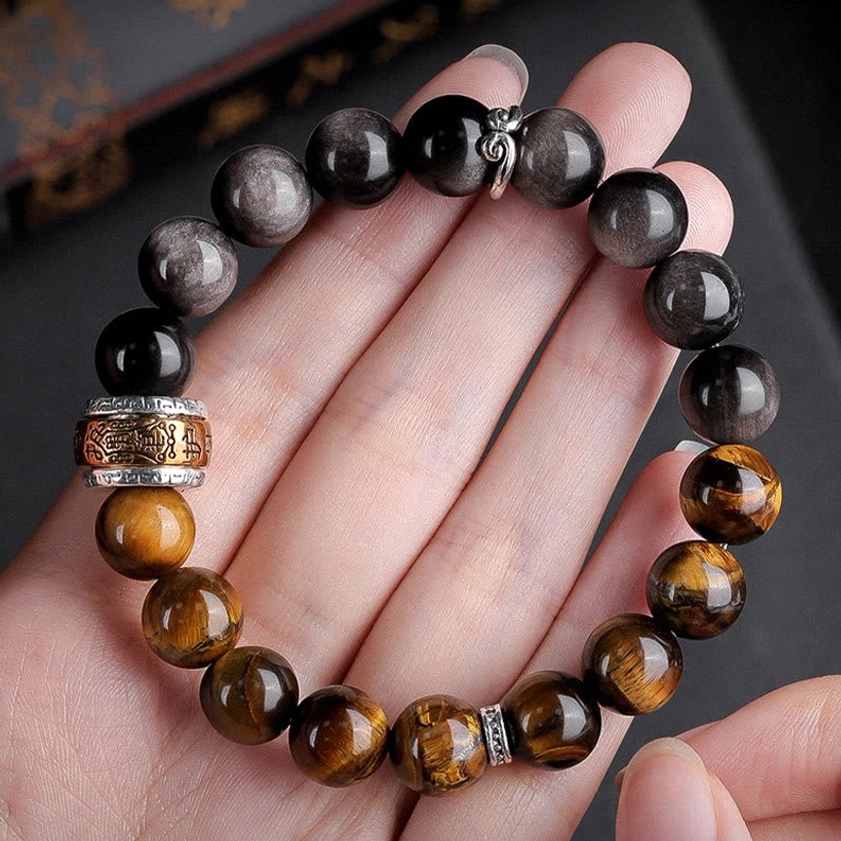 Dual-stone Buddhist beaded bracelet worn on human palm showing detailed view of Silver Sheen Obsidian, Tiger's Eye beads, and metal Om Mani Padme Hum charm