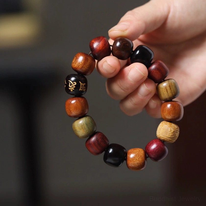Hand-held close-up of natural wood Om Mani Padme Hum bracelet worn on human wrist, showing golden mantra bead and mixed wood construction