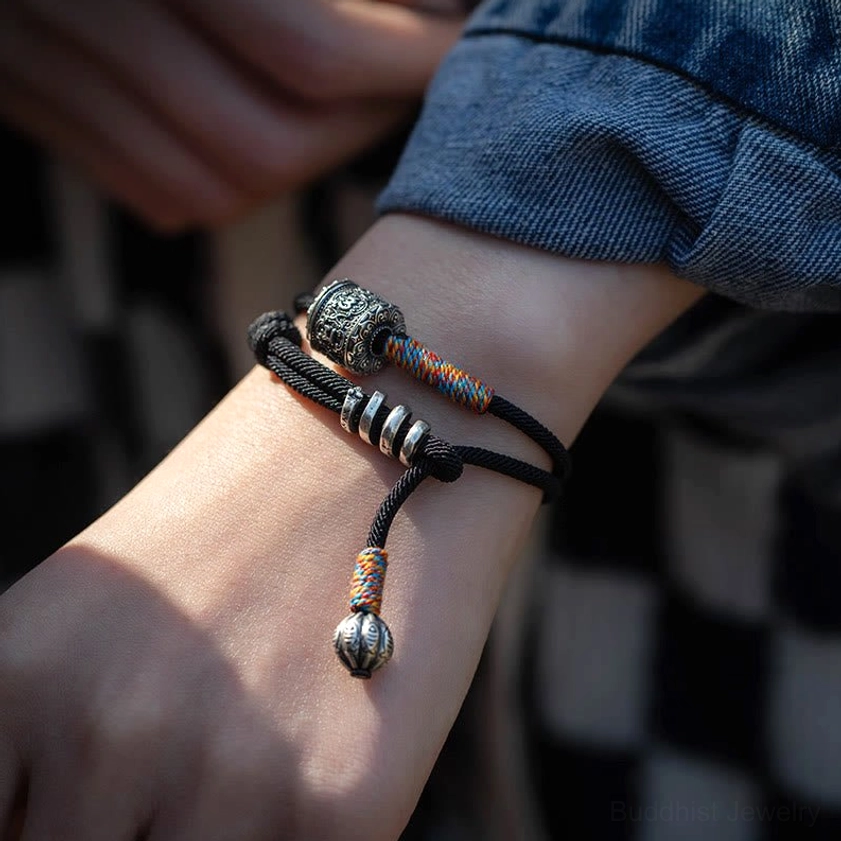 Buddhist meditation bracelet worn on wrist with black braided cord and silver charms in daily casual setting