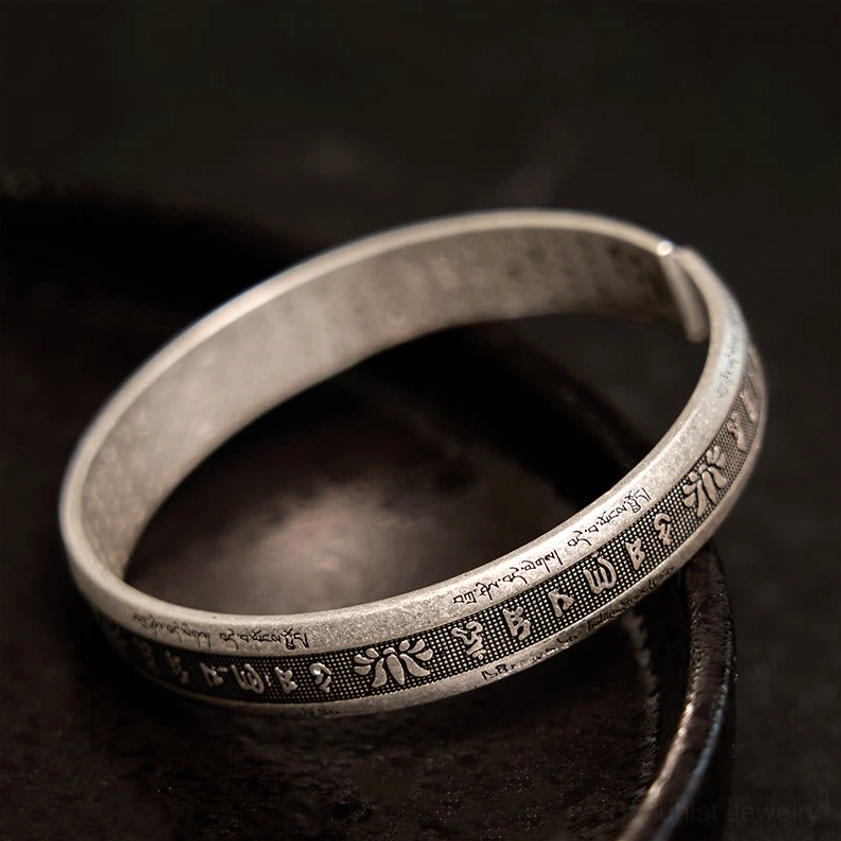 Sacred text meditation cuff bracelet with outer engraved motifs and vintage silver finish, low-angle side view