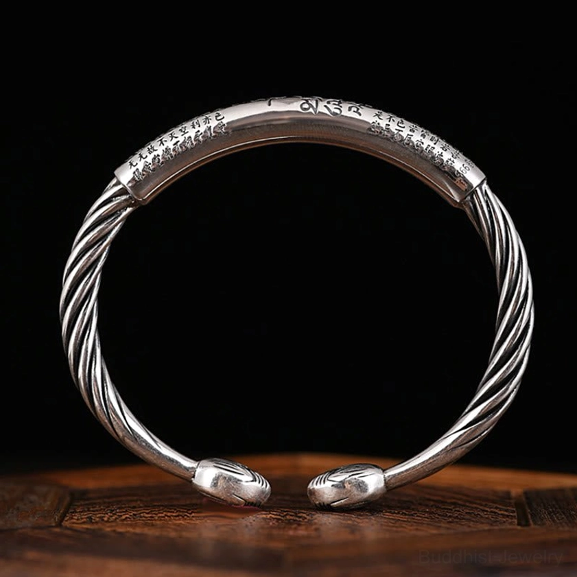 Flat lay overhead view of open-end copper cuff bracelet with full twisted rope band, leaf-shaped end caps, and sacred mantra text in antique silver tone