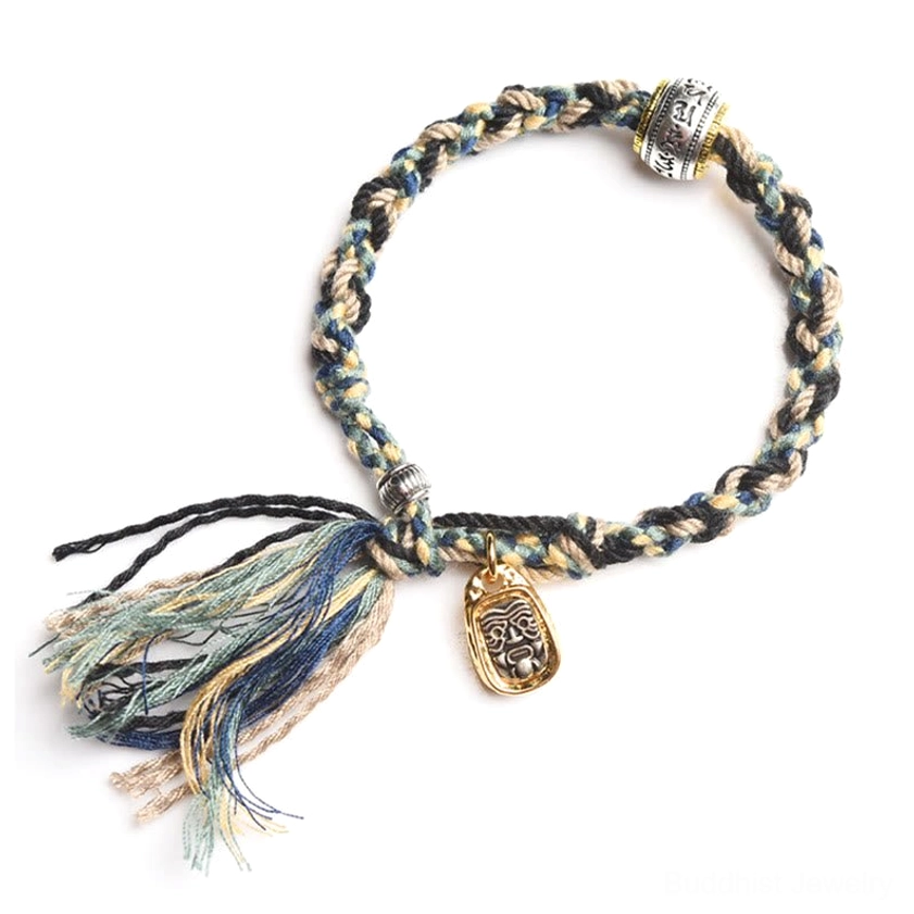 Handmade Buddhist string bracelet with dark mixed-color woven cord, metal charm and barrel bead on white background