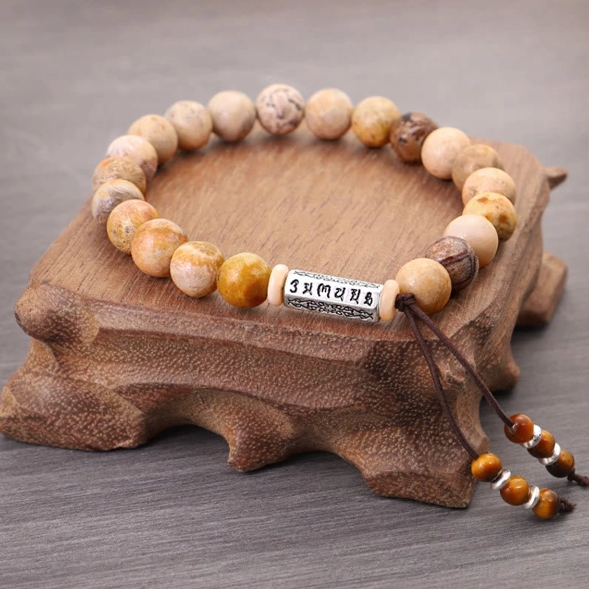 Top-down view of Buddhist weathered stone bracelet on wooden stand showing mantra tag and adjustable cord