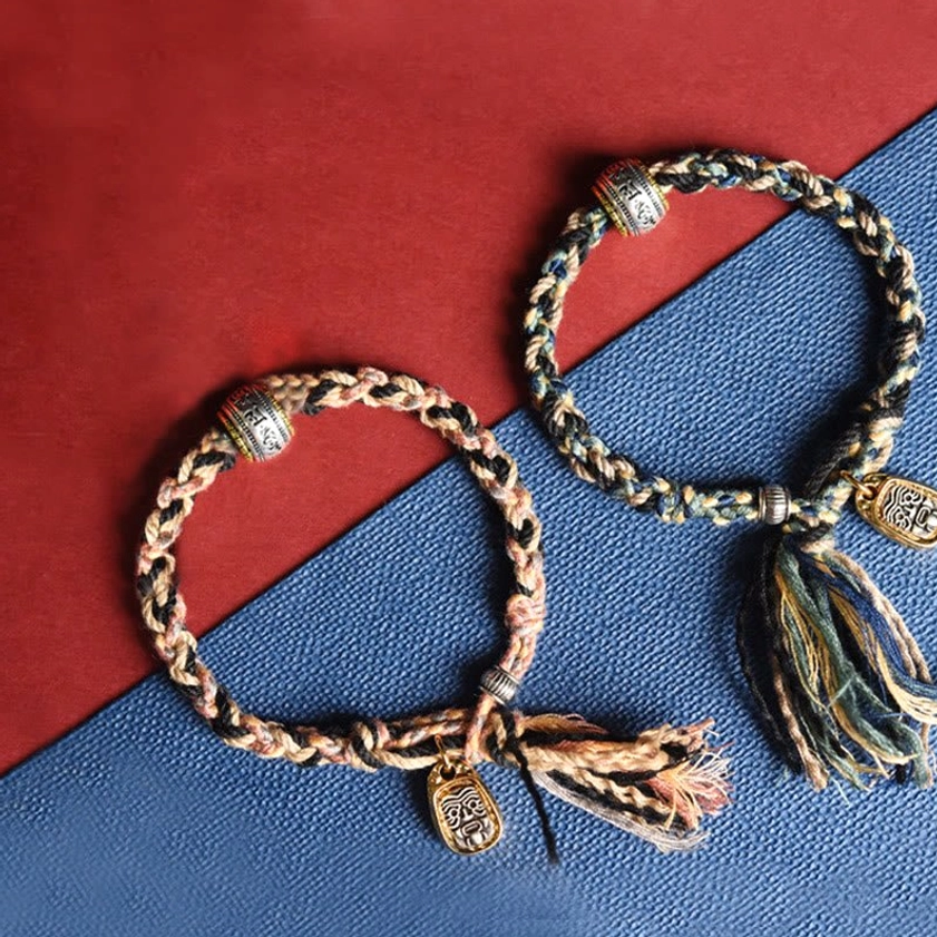 Two matching handmade Buddhist string bracelets with braided cords, metal charms and tassel decorations overhead view