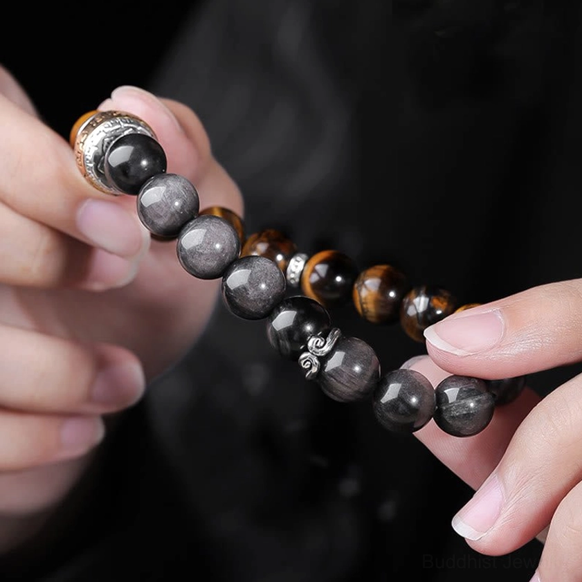 Side view of dual-stone Buddhist bracelet held by hands showing the clasp, elastic cord, and side profile of Silver Sheen Obsidian and Tiger's Eye beads