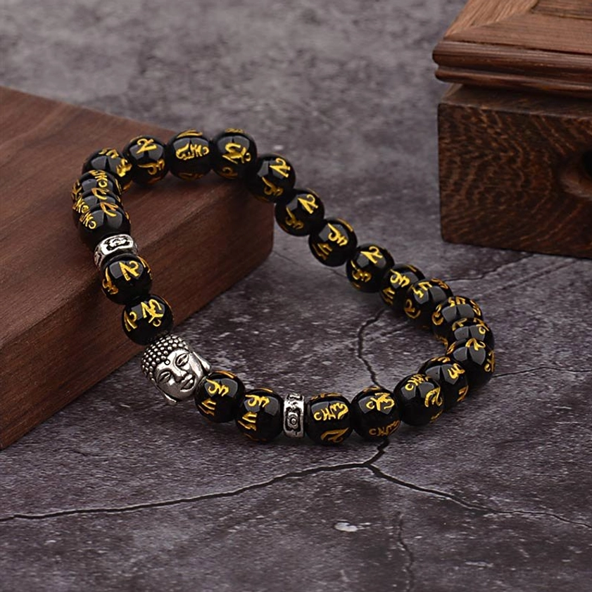 Sacred Sanskrit mantra bracelet with gold engraving and silver Buddha accent, lifestyle photography on wooden surface
