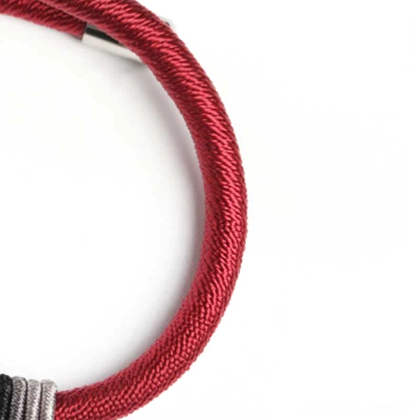 Red cord bracelet detail showing layered gray thread wraps and polished silver hardware