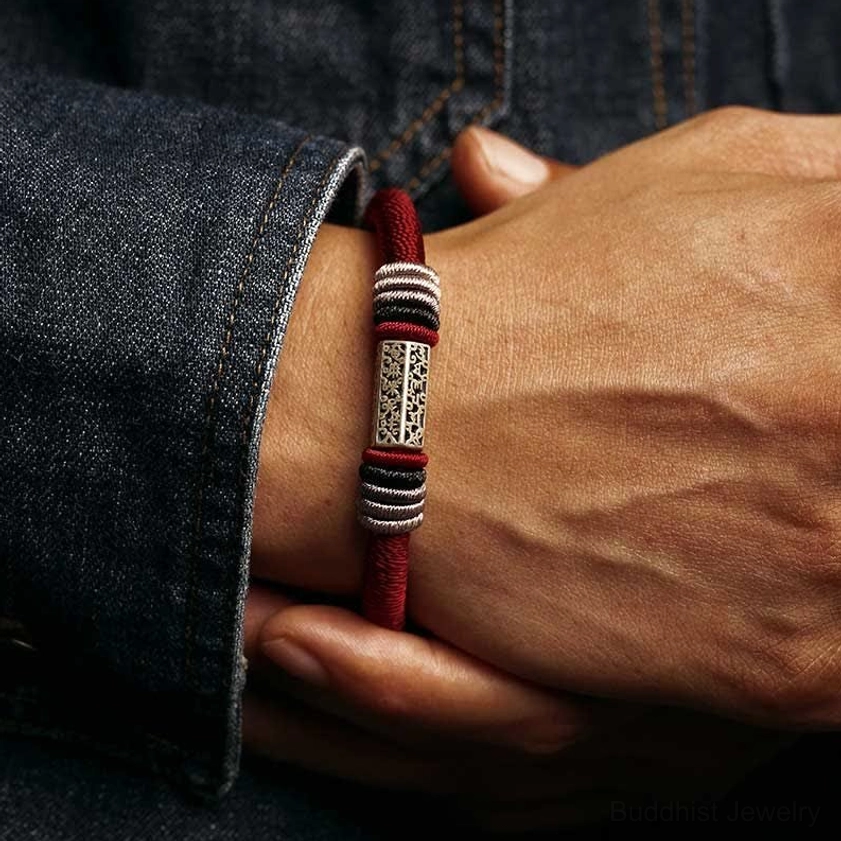Red string bracelet worn on wrist with engraved silver center bead and denim background