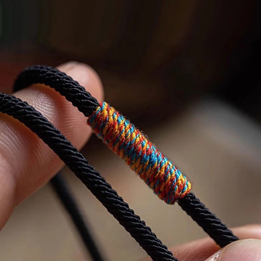 Close-up detail of colorful hand-woven wrap section on black braided Buddhist bracelet cord