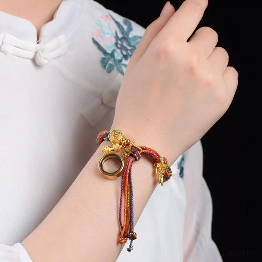 Colorful Buddhist string bracelet worn on wrist showing gold charms and dangling ring pendant in traditional setting