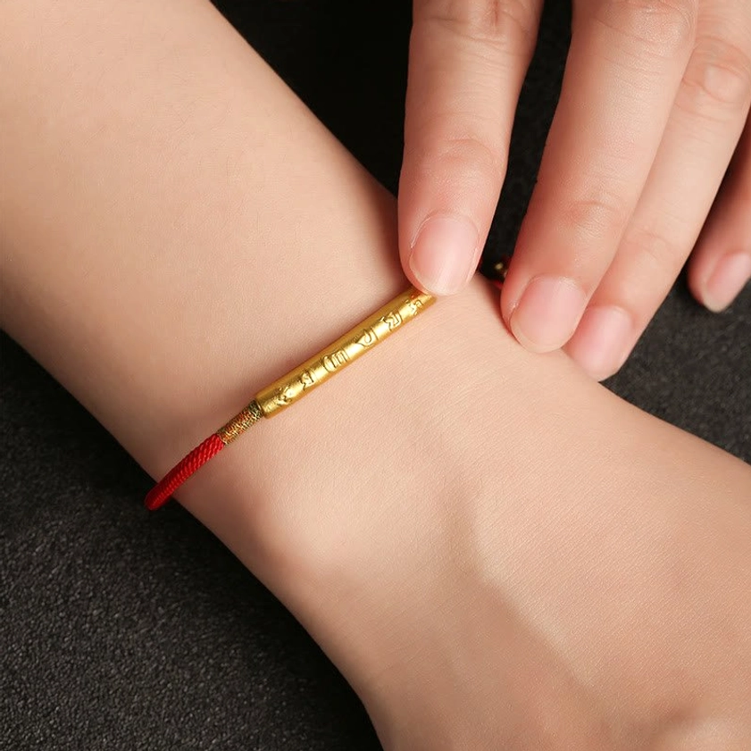 Buddhist red string bracelet worn on wrist, showing adjustable fit with gold engraved tube charm