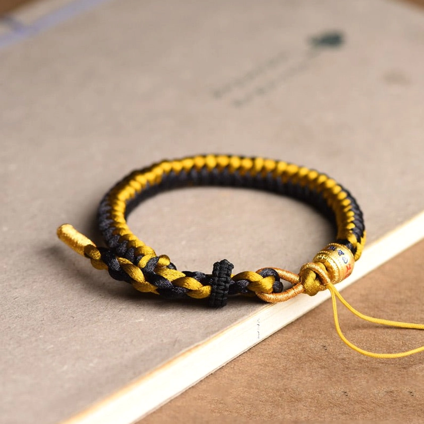 Black and gold braided Buddhist string bracelet with engraved metal bead and yellow adjustable tail cord