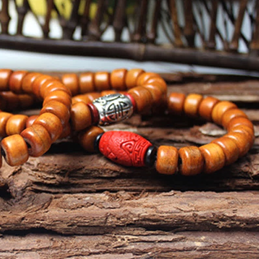Two Om Mani Padme Hum bracelets with barrel beads and red carved charm on rustic wooden surface