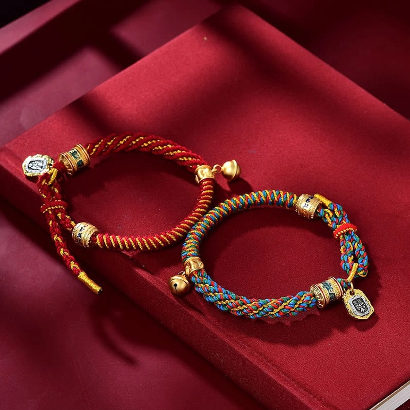 Two Buddhist prayer bracelets featuring red and multicolored braided silk with metal Ghau locket and bell charms