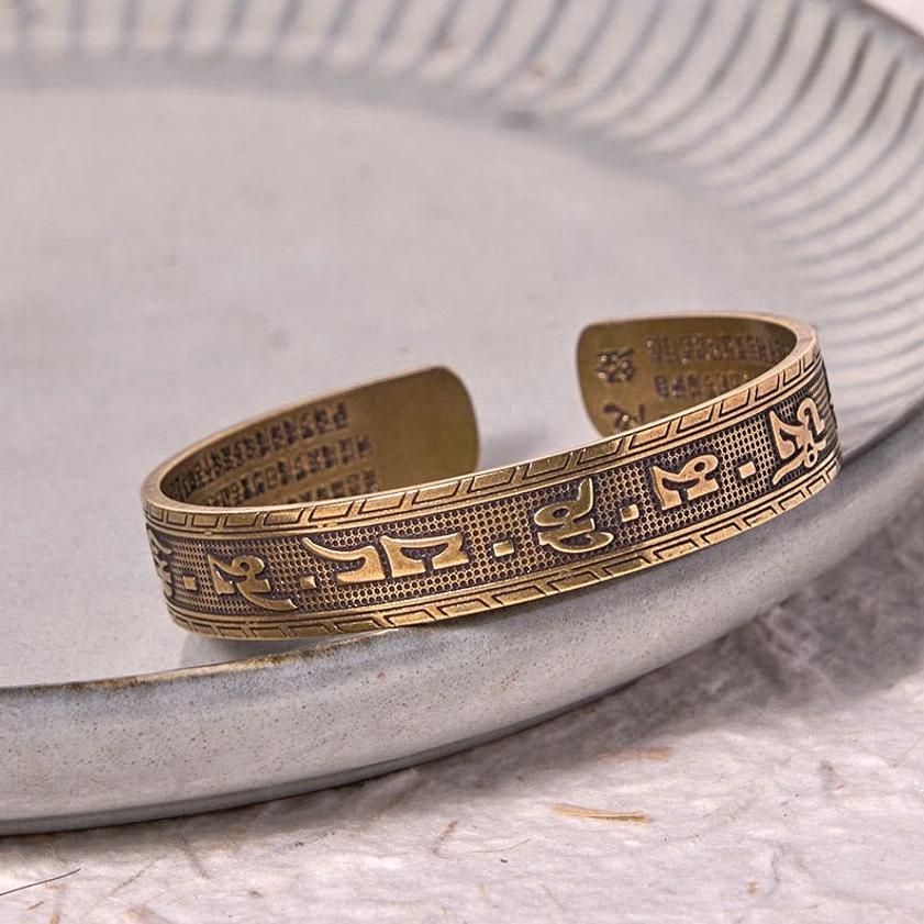 Antique bronze Om Mani Padme Hum brass bracelet with embossed mantras displayed on ceramic plate with geometric edge trim detail