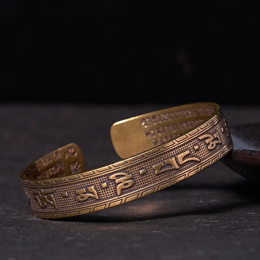 Om Mani Padme Hum brass bangle bracelet with antique bronze finish and embossed six-syllable mantra, viewed from oblique side angle on dark wooden surface