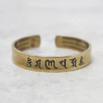 Om Mani Padme Hum brass mantra bracelet with hand-engraved Sanskrit script, polished gold tone open cuff design